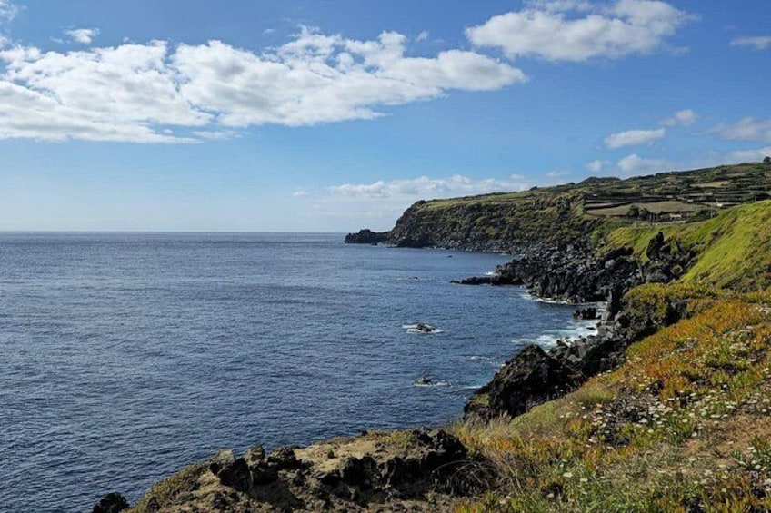 A coastal landscape with a rocky shoreline, grassy hills, and a clear blue sky. 4
