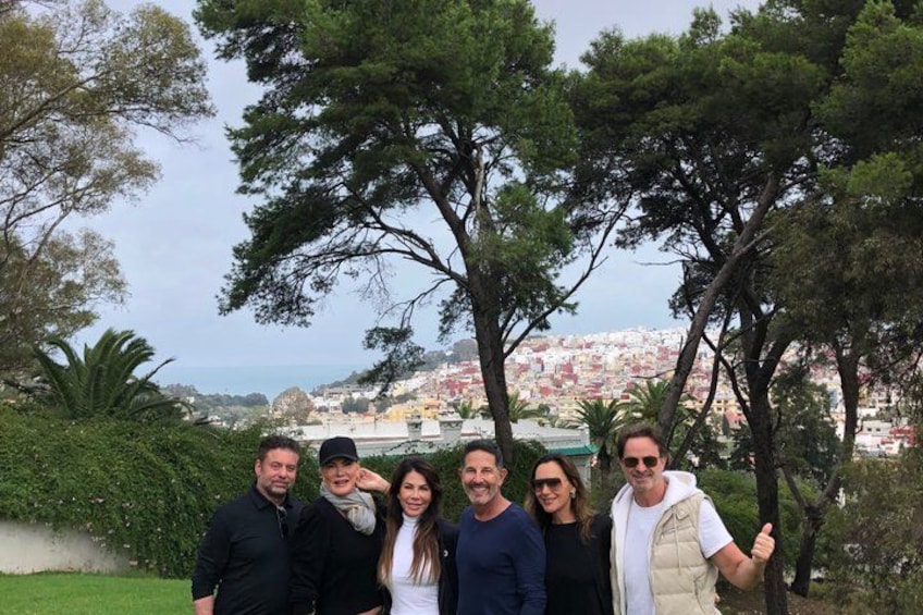 En grupp människor som står i en park med träd och en stadsbild i bakgrunden. 2