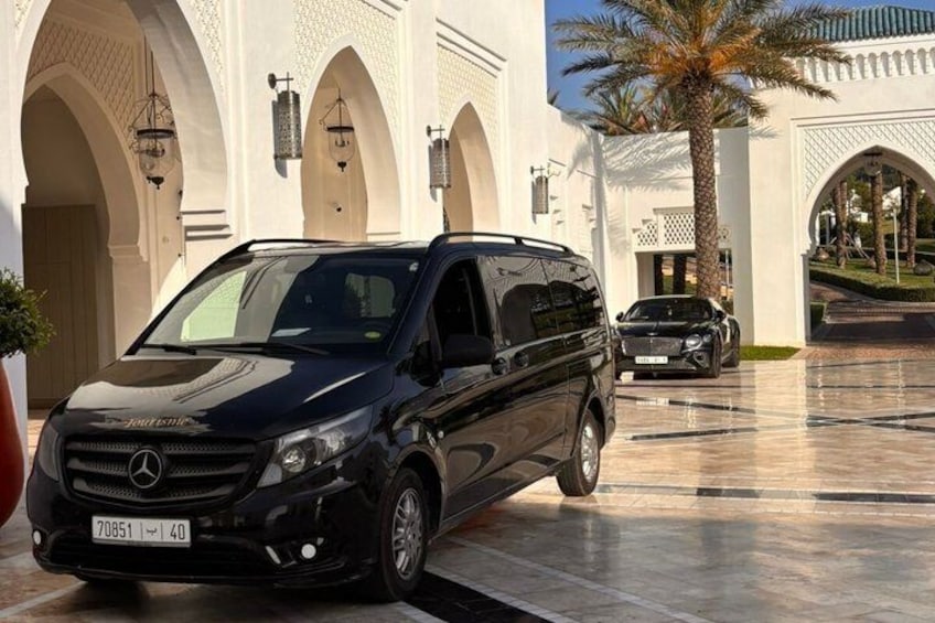 A black Mercedes-Benz Sprinter van parked in a courtyard with arches and palm trees. 4