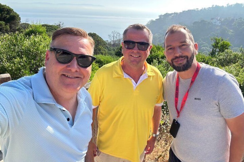 Three people standing outdoors with a hilly landscape in the background. 5