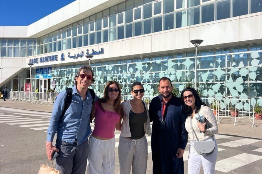 A group of people standing in front of a building with Arabic text. 2