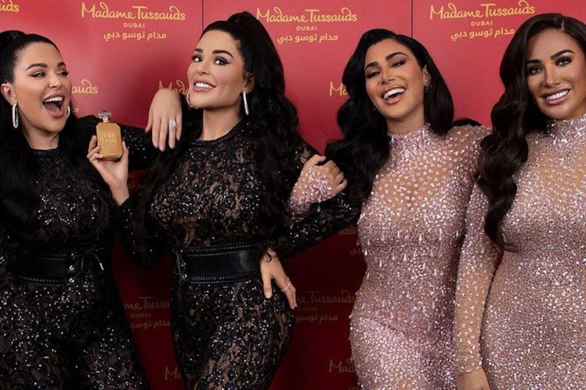 Four women in formal dresses posing in front of a red backdrop with the text 'Madame Tussauds Dubai'. 1