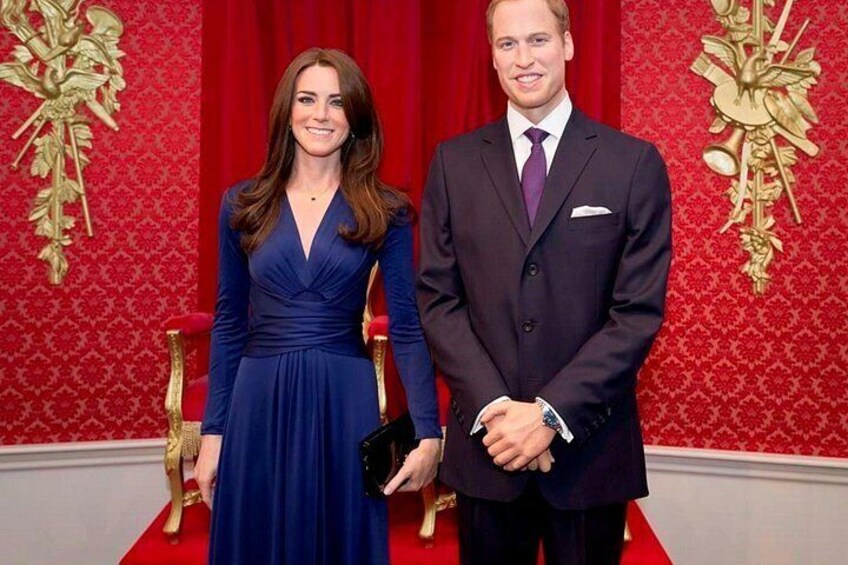 A person in a dark suit and a woman in a blue dress standing in front of a red curtain with gold designs. 4