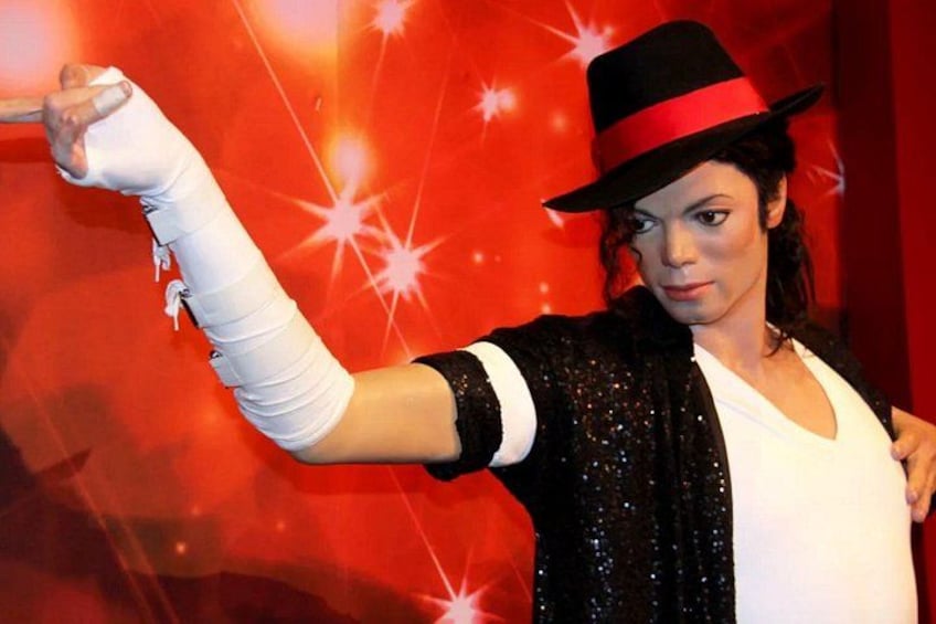 A person with a cast on their arm, wearing a hat and a sequined jacket, against a red background with star-like light effects. 2