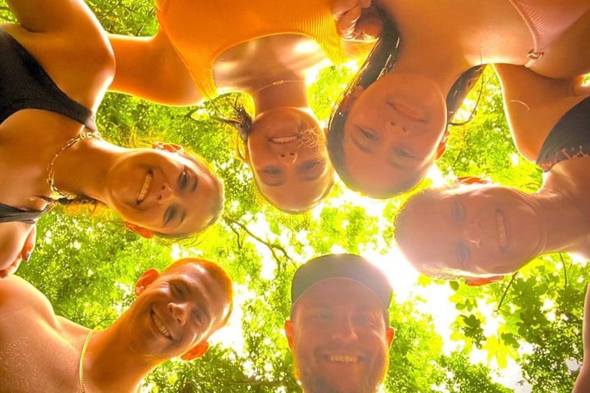 Een groep mensen staat buiten in een kring, met bomen op de achtergrond. 1