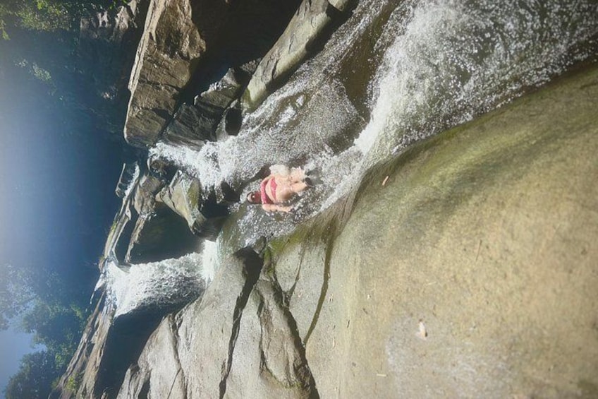 Een persoon in een rood badpak staat op een rots nabij een waterval. 4