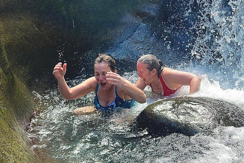 Twee mensen zwemmen in een natuurlijk waterlichaam, omringd door rotsen. 3