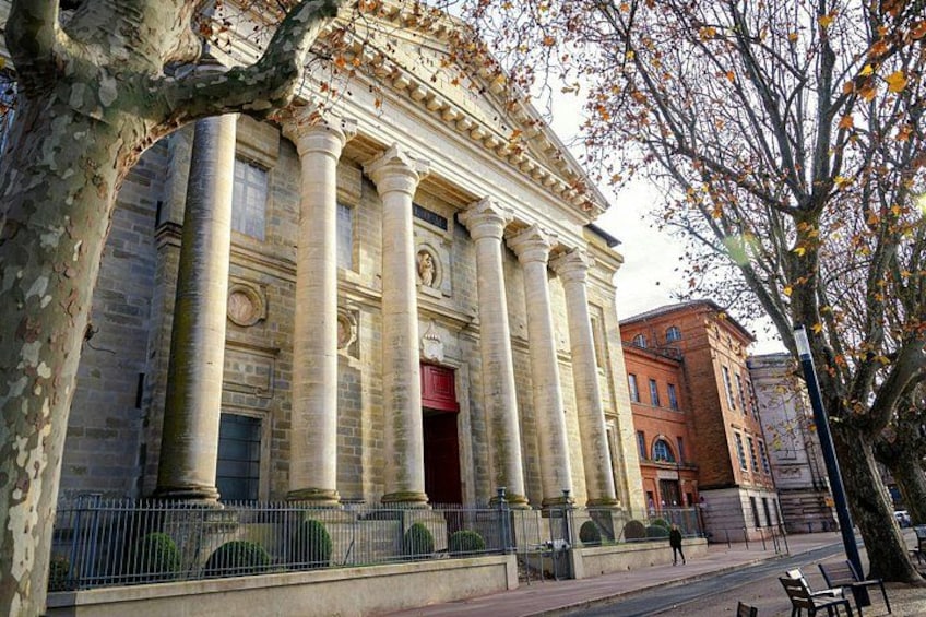 A classical building with columns, a red door, and a tree with autumn leaves. 4