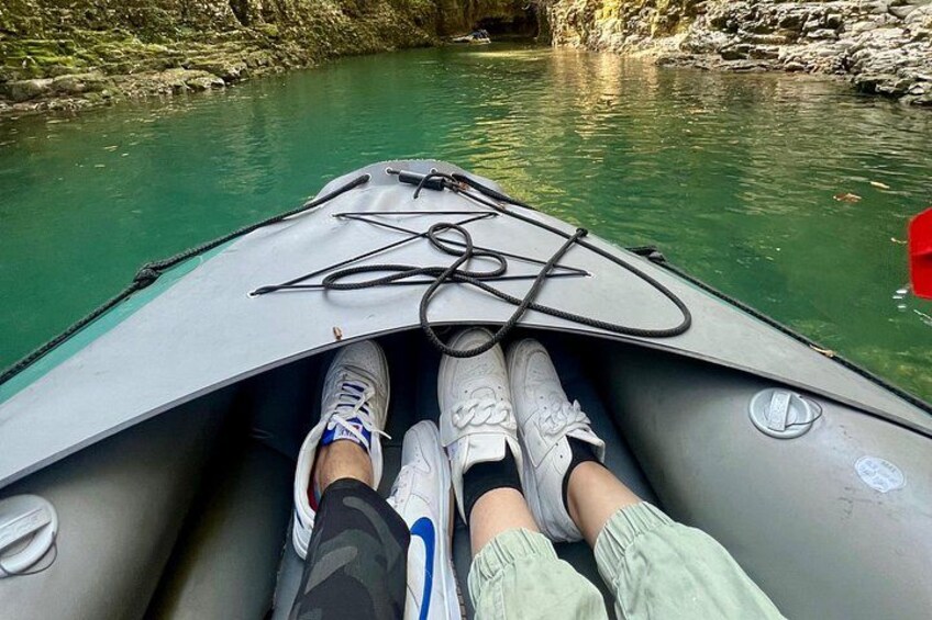 Une personne assise dans un bateau sur une rivière, avec une végétation luxuriante et des rochers en arrière-plan. 2