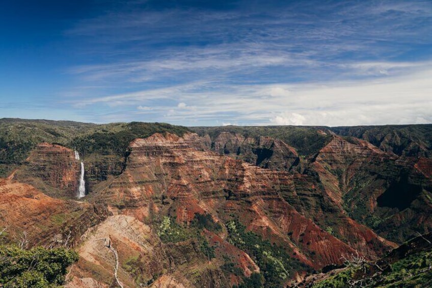 A canyon with a waterfall and layered rock formations. 1
