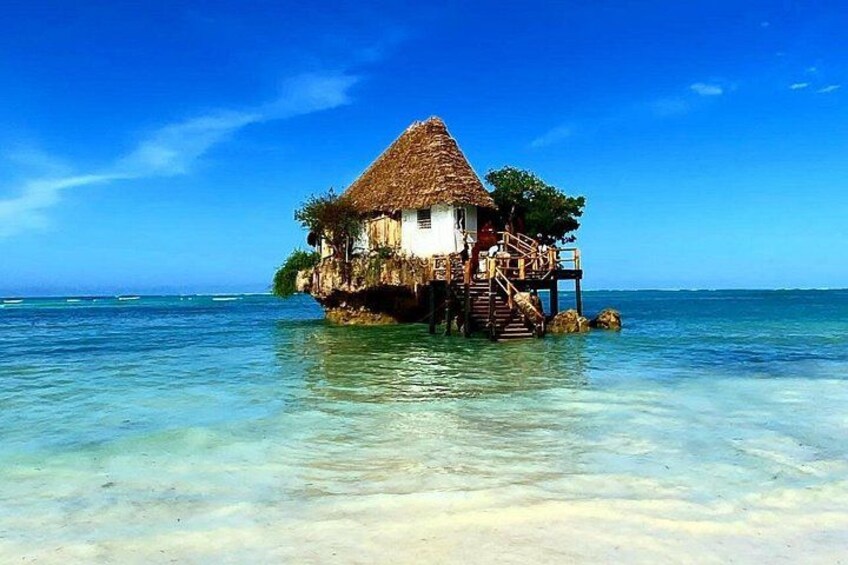 A thatched-roof house on stilts over clear turquoise water. 1