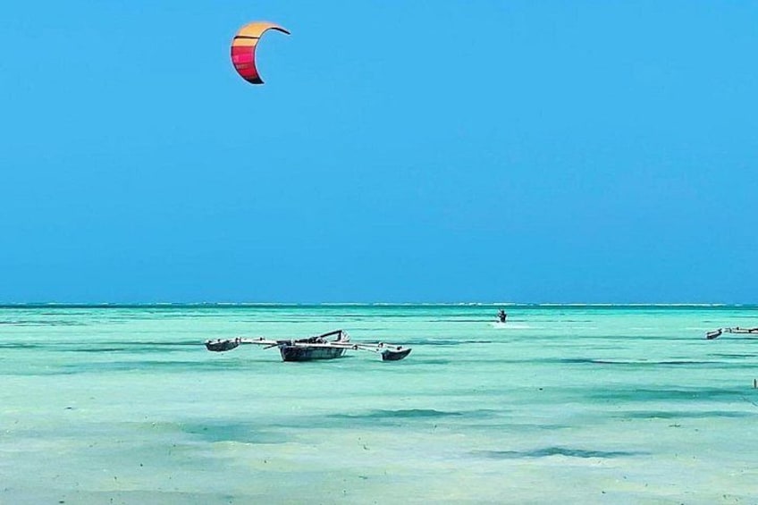 A clear blue sea with a parasail, a small boat, and a distant person. 3