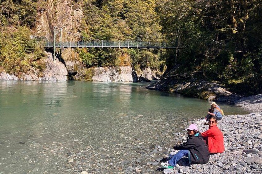 A river with a bridge, rocky shore, and people sitting on the rocks. 2
