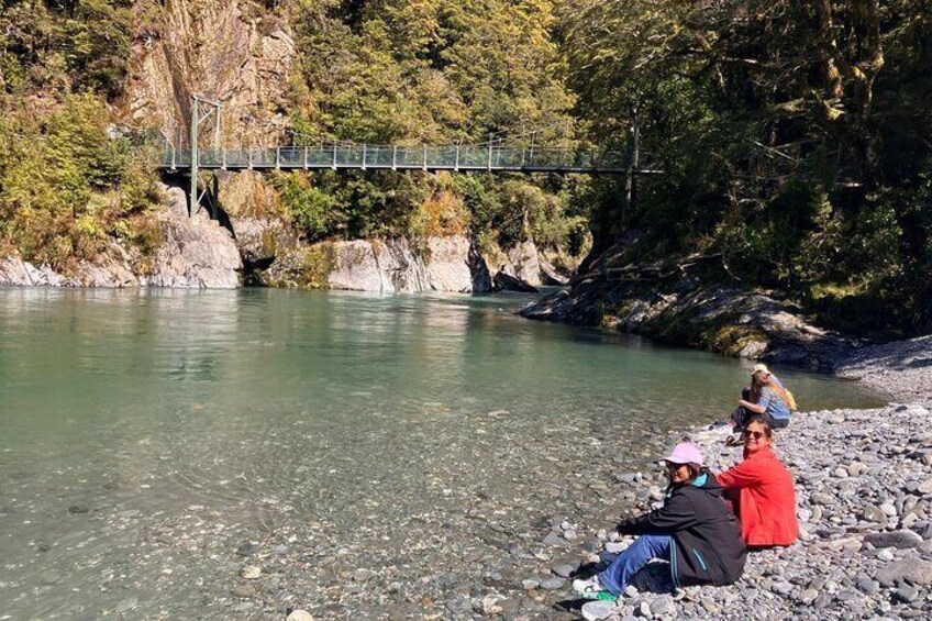A river with a bridge, rocky shore, and people sitting on the rocks. 5