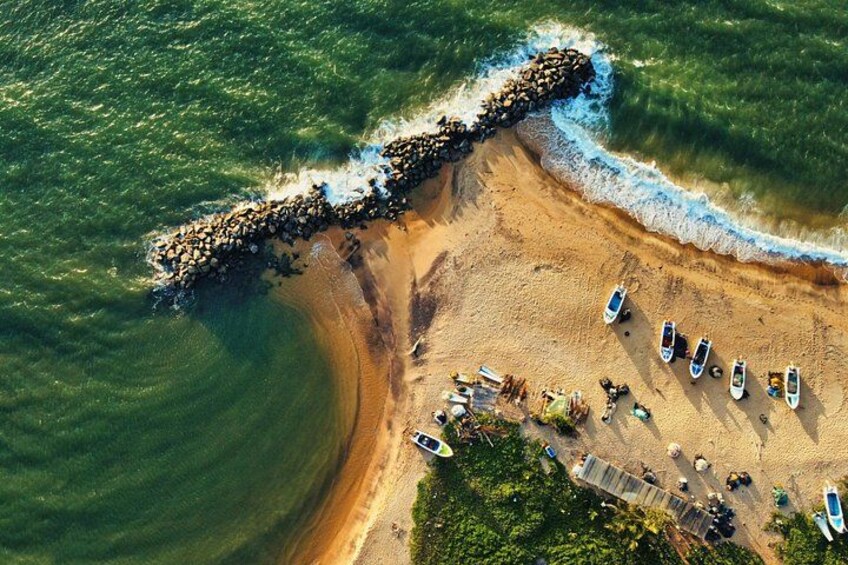 An aerial view of a beach with boats, a rocky breakwater, and a sandy shore. 5