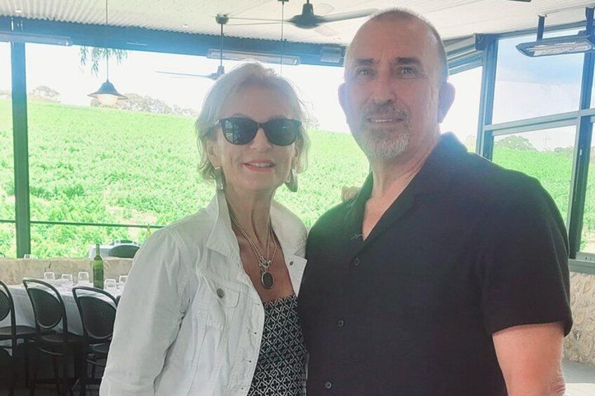 Two people standing indoors with a view of a green field outside. 1