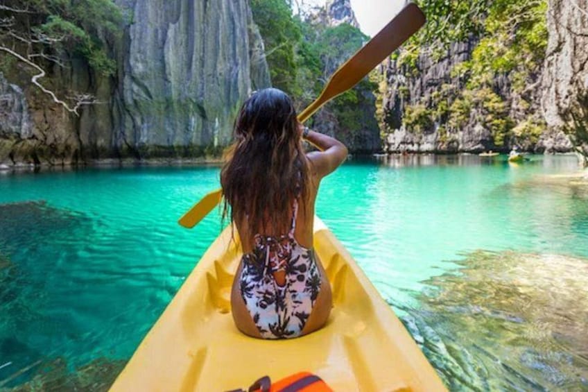 Una persona en un kayak amarillo rema por aguas turquesas y transparentes, rodeada de acantilados rocosos. 2