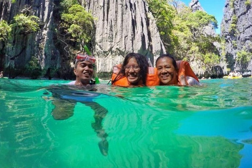 Tres personas en agua cristalina, con acantilados rocosos al fondo. 3