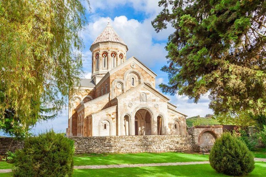 A historic church with a bell tower, surrounded by greenery and stone walls. 2