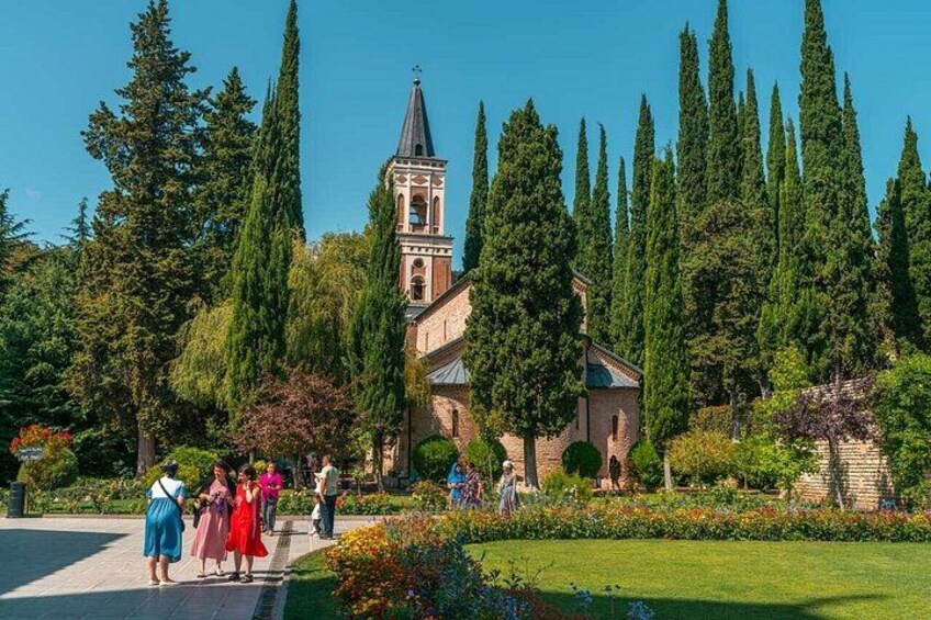 A church with a bell tower, surrounded by tall trees and a well-maintained garden. 4