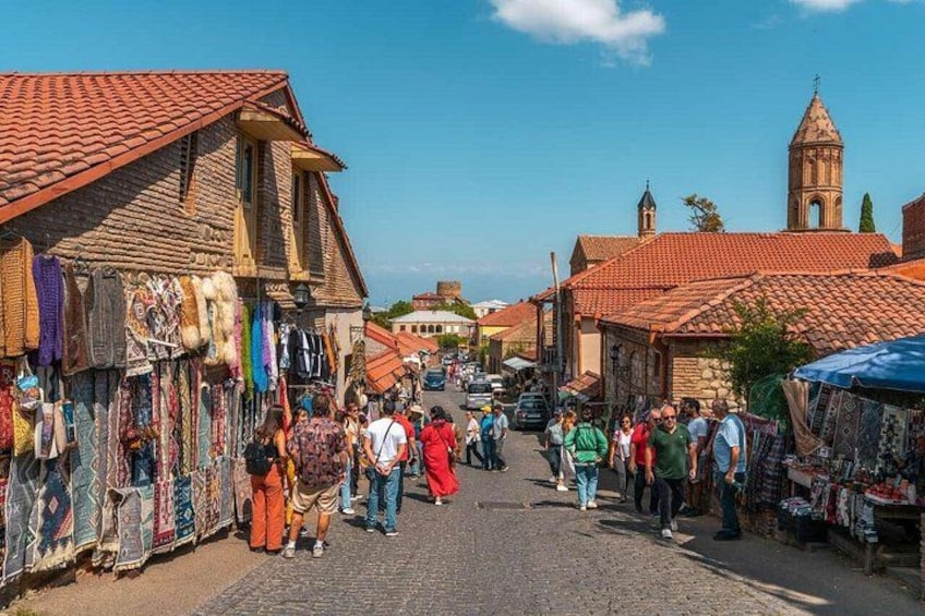 A cobblestone street lined with shops and a church tower in the background. 2