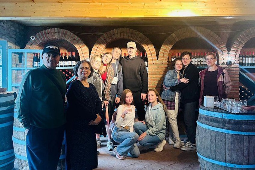 A group of people inside a brick-walled cellar with wine barrels. 2