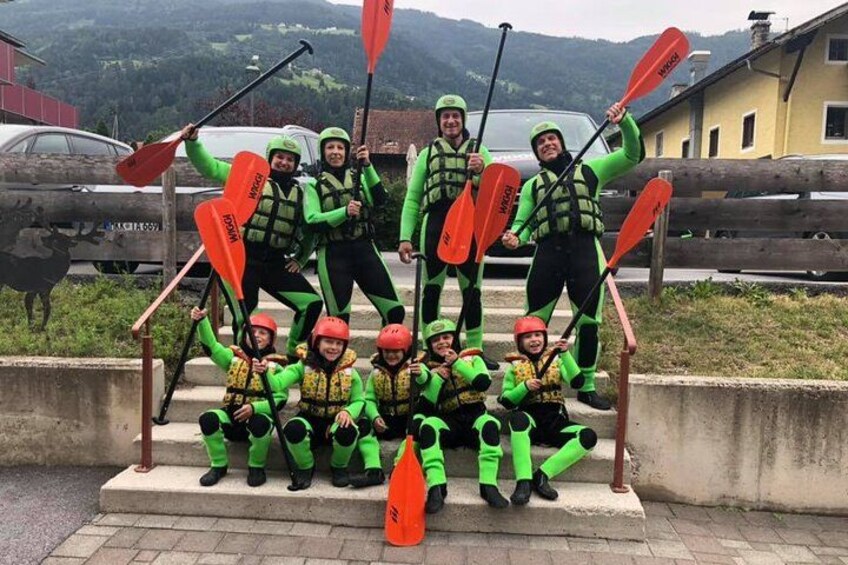 A group of people in green and yellow life jackets posing with paddles on steps. 3