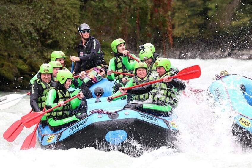 A group of people in a blue inflatable raft with red paddles, navigating through a body of water surrounded by trees. 5