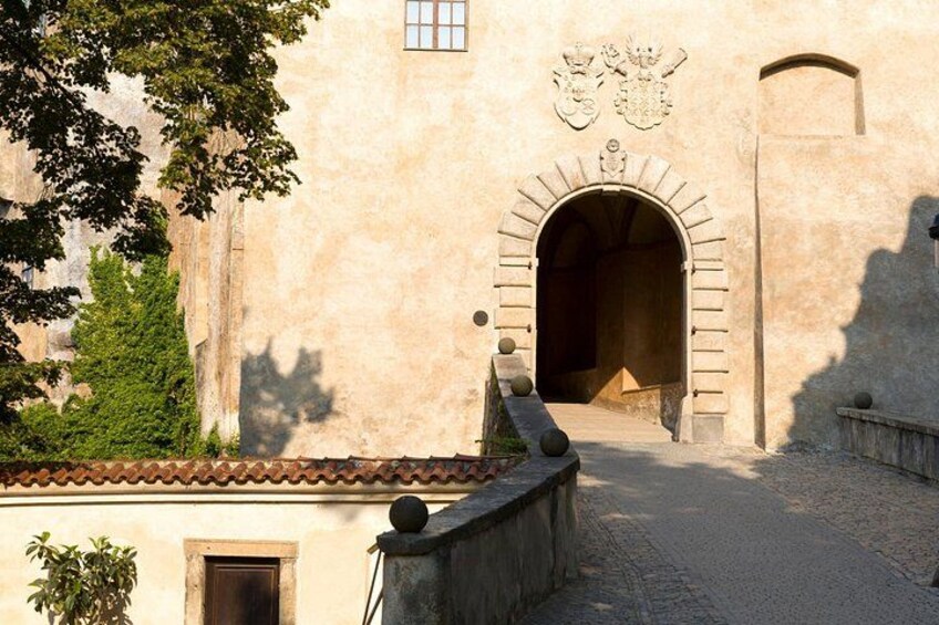 A stone building with an arched entrance, a tiled roof, and a tree in the foreground. 4