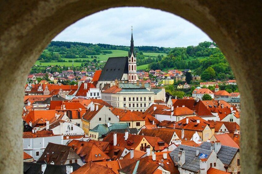 A town with red-roofed buildings, a prominent church with a tall spire, and a green landscape in the background. 5