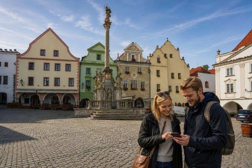 A cobblestone square with historic buildings, a central fountain, and a couple using a smartphone. 3