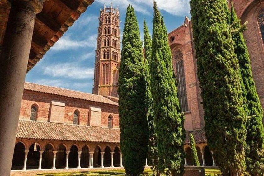 A historic building with a tall tower, arched walkways, and tall cypress trees. 3