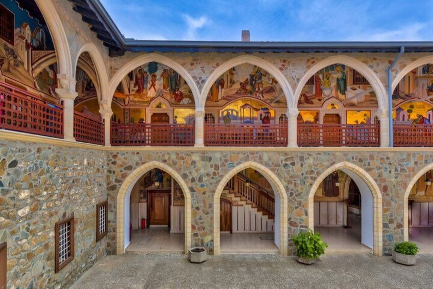 Une cour bordée de murs en pierre, dotée de plusieurs arcades et d’un balcon avec des balustrades rouges. 1