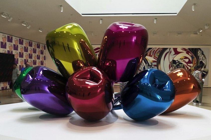 Een verzameling kleurrijke glazen sculpturen op een wit voetstuk in een galerie. 2