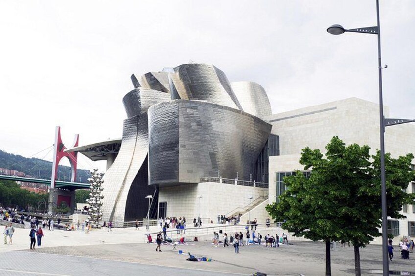 A modern architectural building with a unique, curved design, surrounded by a public square with people and a red bridge in the background. 4