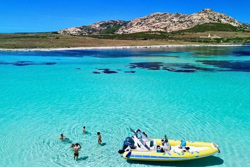 A clear turquoise sea with a yellow inflatable boat and people swimming. 1