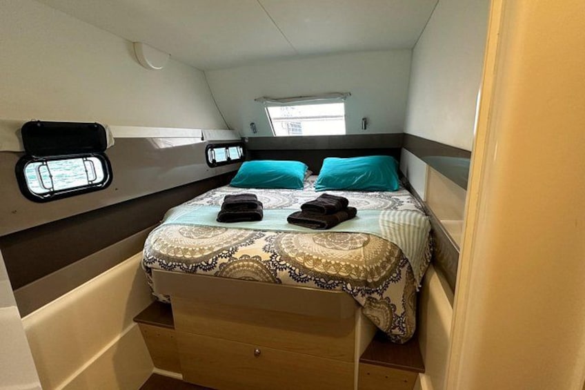 Een knus slaapkamer met een bed, twee kussens, een raam en een klein opbergkastje. 2