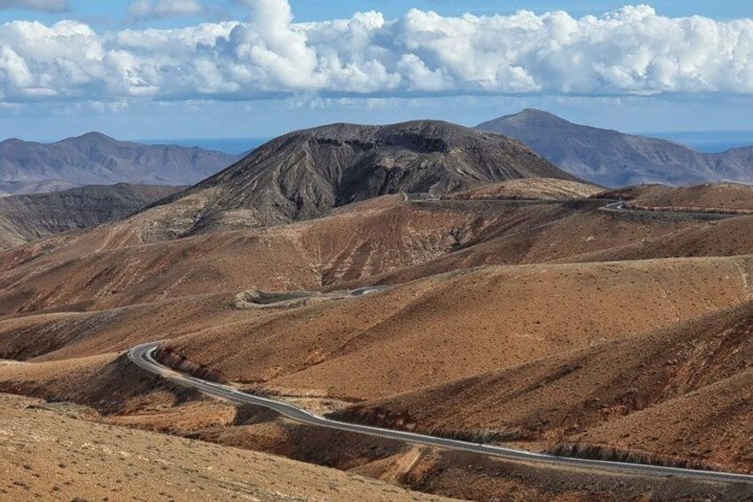 Una carretera sinuosa en la montaña, terreno rocoso y montañas distantes bajo un cielo parcialmente nublado. 2