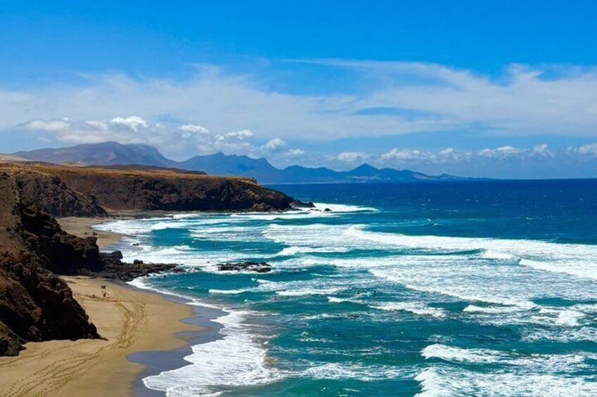 Eine Küstenlandschaft mit Sandstrand, Felsen und einem klaren blauen Ozean. 4