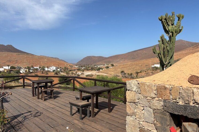 A wooden deck with tables and benches overlooking a desert landscape with mountains and a cactus. 4