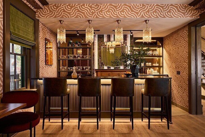 Eine Bar mit strukturiertem Wandpapier, hölzernen Barhocker und hängenden Kristallleuchtern. 4