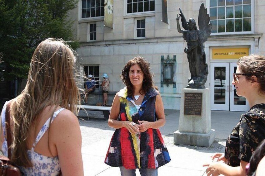 Drei Frauen stehen draußen vor einem Gebäude mit einer Statue und einem Schild, auf dem 'Ashville Art Museum' steht. 1