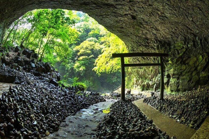 A cave entrance with a wooden walkway, rocky terrain, and lush greenery. 2