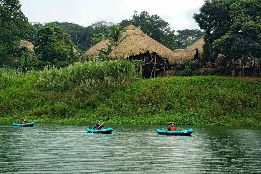 Three kayaks on a calm river with thatched-roof huts in the background. 2