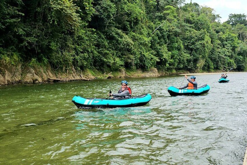 Trois personnes pratiquent le kayak sur une rivière bordée d’une végétation luxuriante. 1