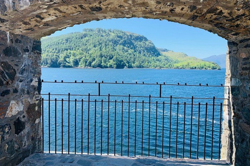 Ein Steingewölbe mit Metallgeländer, das auf einen See und einen bewaldeten Hügel blickt. 4