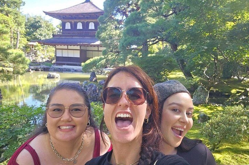 Three people in front of a traditional Japanese building with a pond and trees. 1