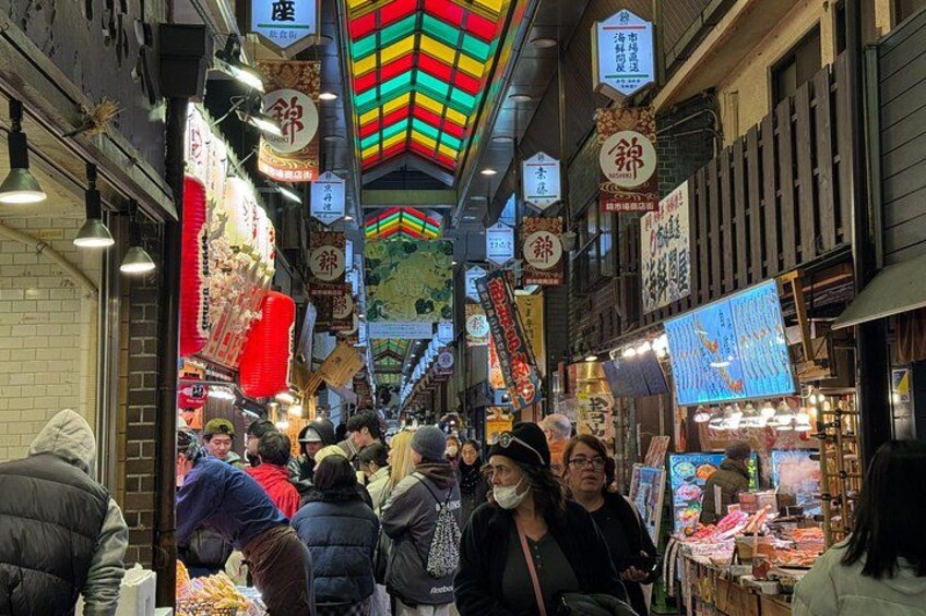 A bustling indoor market with people shopping, colorful signs, and traditional decorations. 2