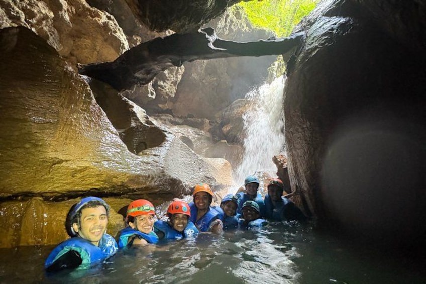 A group of people in blue life jackets in a water-filled cave with a waterfall. 4