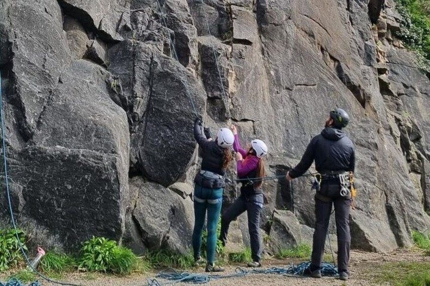 Un grupo de personas practica escalada en roca con una pared rocosa imponente al fondo. 2